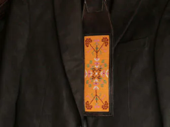 Leather tie is hanged onto the hanger with the gentleman's jacket. The beadwork on the centre of the tie is mostly yellow and features Estonian folk pattern.