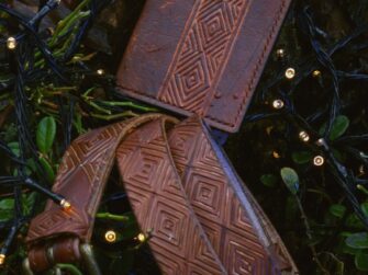 Leather goods are presented on the tree trunk background. There are some forest plants surrounding the items and also some small sparkling little lights as a decoration.