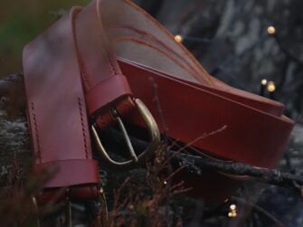 Belts are placed onto the fallen tree trunk in the midst of green and red-brown forest plants. Some small sparkling electrical lights have been used to decorate the scene so there are small little lights surrounding the belts from the right side of the image. On the left upper side of the image there are also some farther threes vaguely visible through the bokeh effect and it gives a nice deepness to this photo.