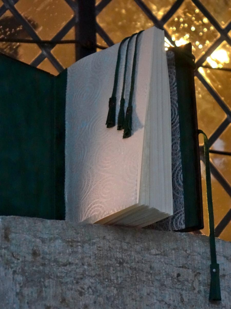 Opened book is placed onto the stained glass window sill. There is a warm yellow light shining through the window.