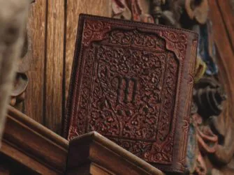 Leather covers displayed on the wooden panel. Panel is carved and painted in multiple colors. this photo features the back side of the covers.