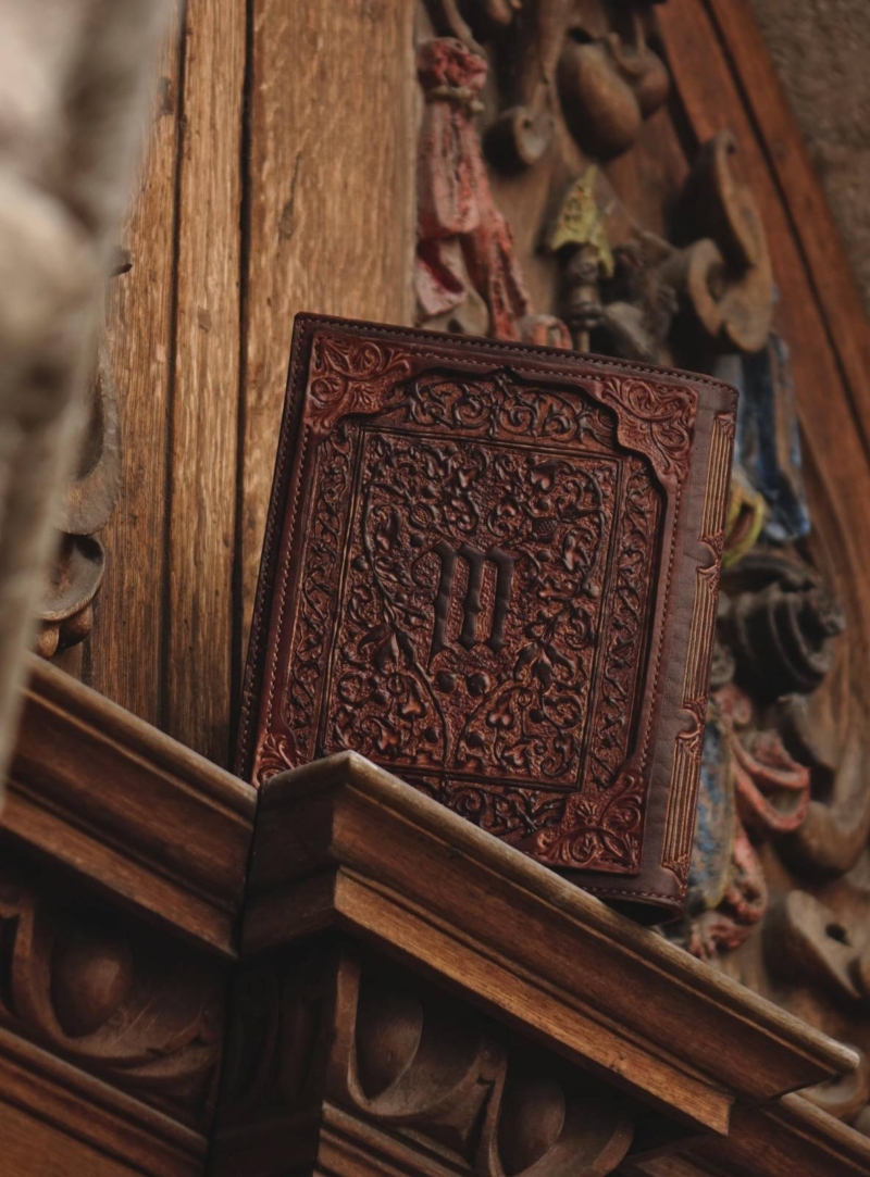 Leather covers displayed on the wooden panel. Panel is carved and painted in multiple colors. this photo features the back side of the covers.