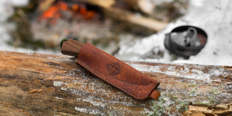 Knife sheath on the snowy tree trunk, bonfire on the background.