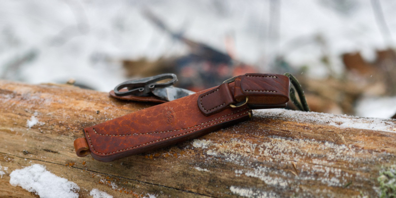 Knife sheath on the snowy tree trunk, bonfire on the background.