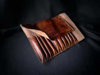 Brown leather tools roll photographed on the black canvas background. The roll is opened and all the inner pockets are visible.