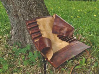 This photo shows the knife roll opened in full size. Leather roll is placed onto the grass besides a tree which is supporting it behind.