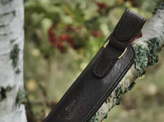 Knife sheath in on the white birch branch, red and green colored rowan branches on the background. The focus of this photo is on the back side of the sheath.