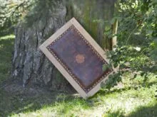 Leather seat cover, decorated by hand carved symbol, is attached to the wooden seat by furniture nails. There is also some cushioning between the wood and leather. 