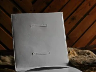 White leather covers for vinyl record, photographed indoors. Covers are placed onto hairy skin, opened towards the viewer. There is a pocket on the inside and a vinyl record is in it. Also, there is a curious frame on the other side of the covers.