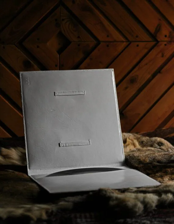 White leather covers for vinyl record, photographed indoors. Covers are placed onto hairy skin, opened towards the viewer. There is a pocket on the inside and a vinyl record is in it. Also, there is a curious frame on the other side of the covers.