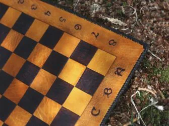 This photo shows a close up of the chess board markings and checkers. The markings are carved in medieval style font. The main colour of the board is yellow and the alternating is dark brown.