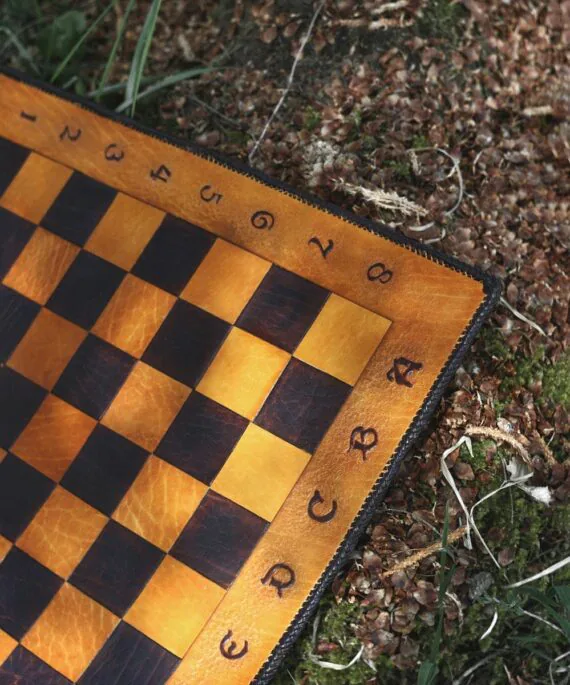 This photo shows a close up of the chess board markings and checkers. The markings are carved in medieval style font. The main colour of the board is yellow and the alternating is dark brown.