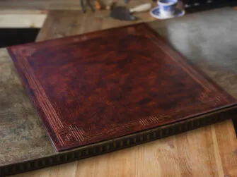 Photo shows an installed leather desk pad on the antique desk's top. Desk's top is dark brown and pad is dyed in mahogany. Leather desk pad is decorated by hand carved frame.