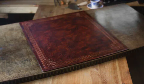 This desk pad is glued onto the special wooden insert this sort of desks usually have. This way it sits right in the desk's top and is made to be as even as possible to match the surrounding height of the desktop itself. Made out of vegetable tanned leather, decorated by carved art-deco style framing. 