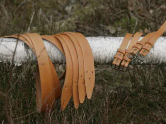 Leather straps are set onto the fallen birch tree trunk. The straps are in various sizes, natural color.