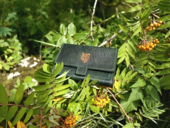 Wallet placed onto tree branches. Lots of green leaves and berries around it.